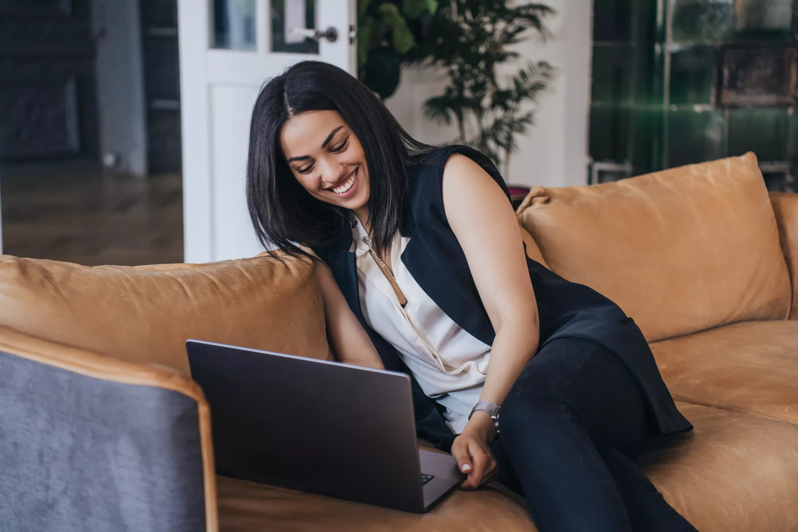 A smiling young woman engaging in a video chat on her laptop, enjoying a fun and interactive online conversation.